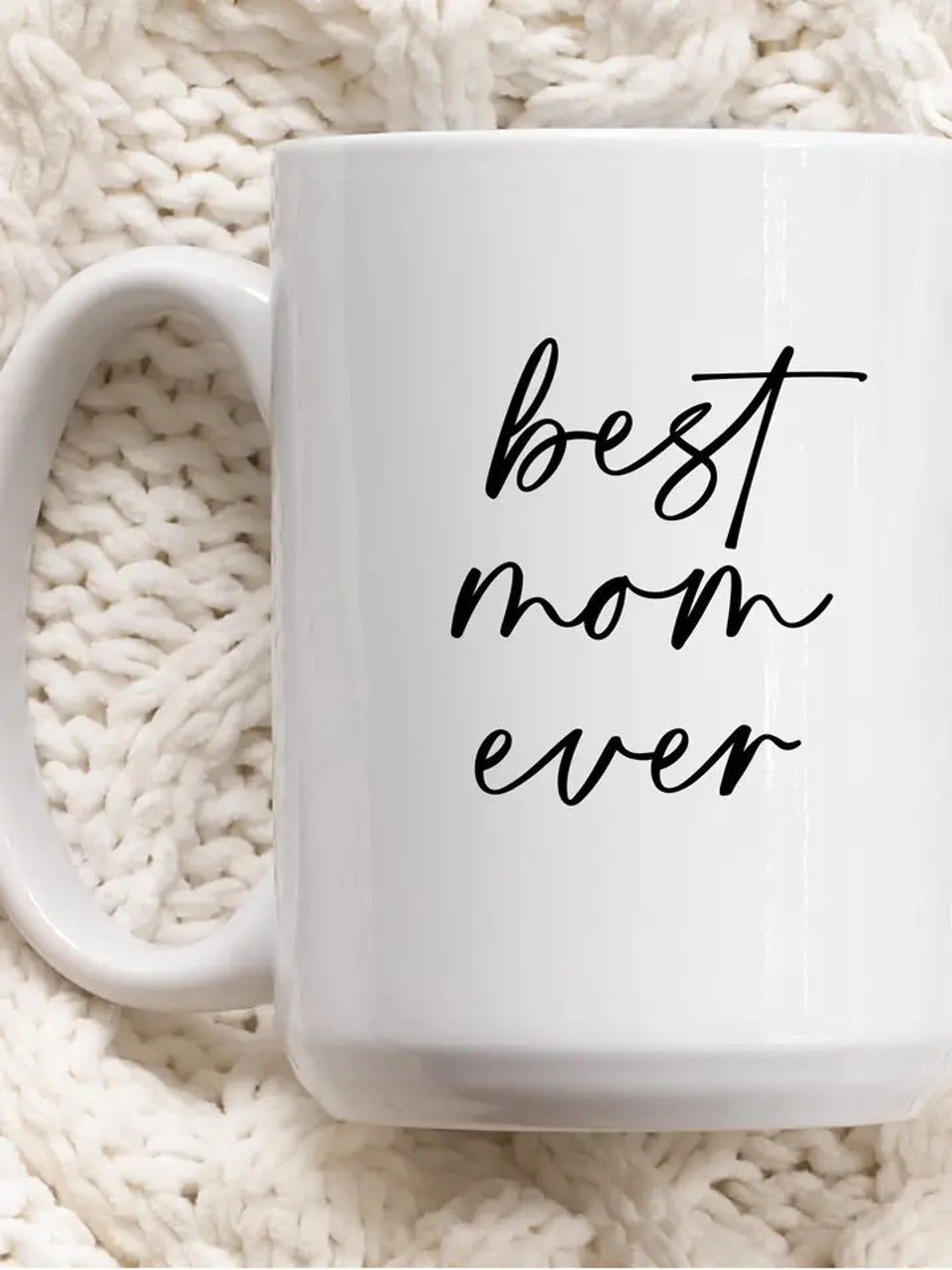 White mug with 'best mom ever' text on a white knitted background